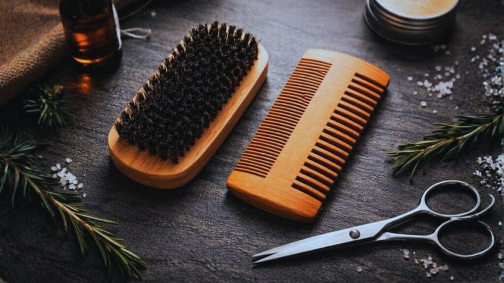 Wooden beard brush and beard comb arranged on a dark textured surface with grooming tools.
